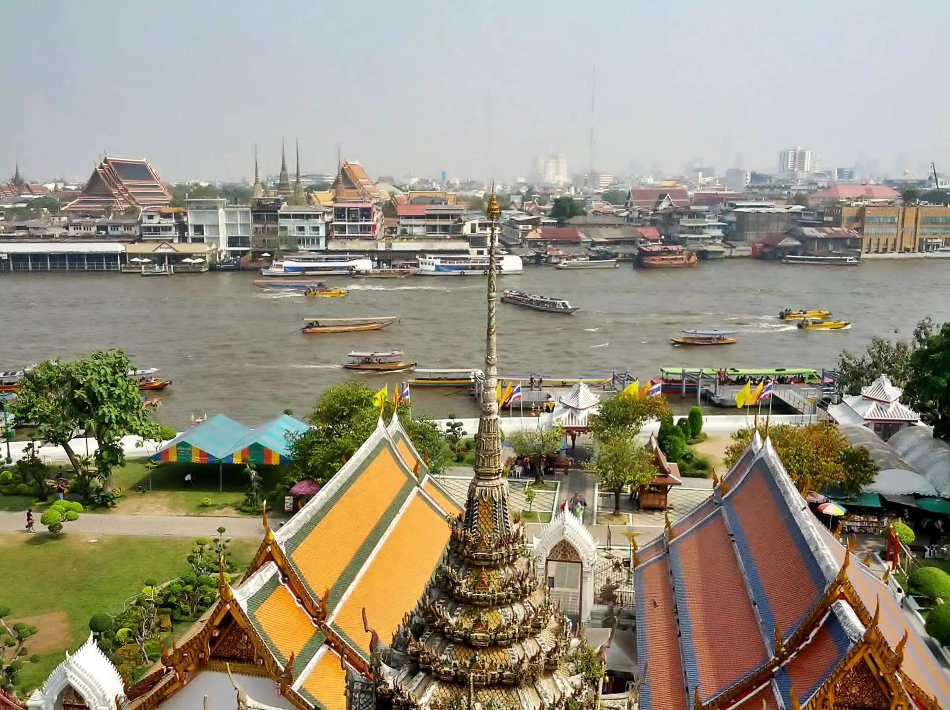 Boats on the Chao Phraya River with temple roofs and the far bank beyond