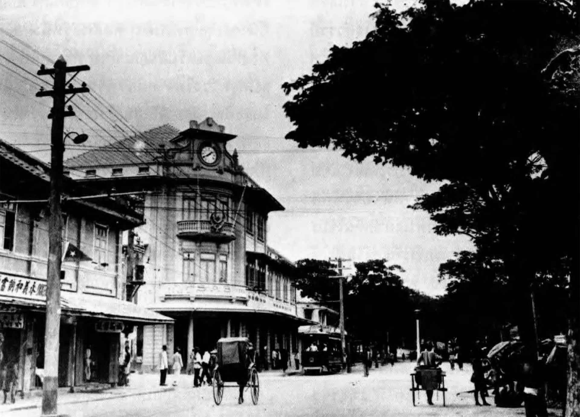 Black-and-white historic photograph of Charoen Krung Road with a clock-tower corner building and rickshaws