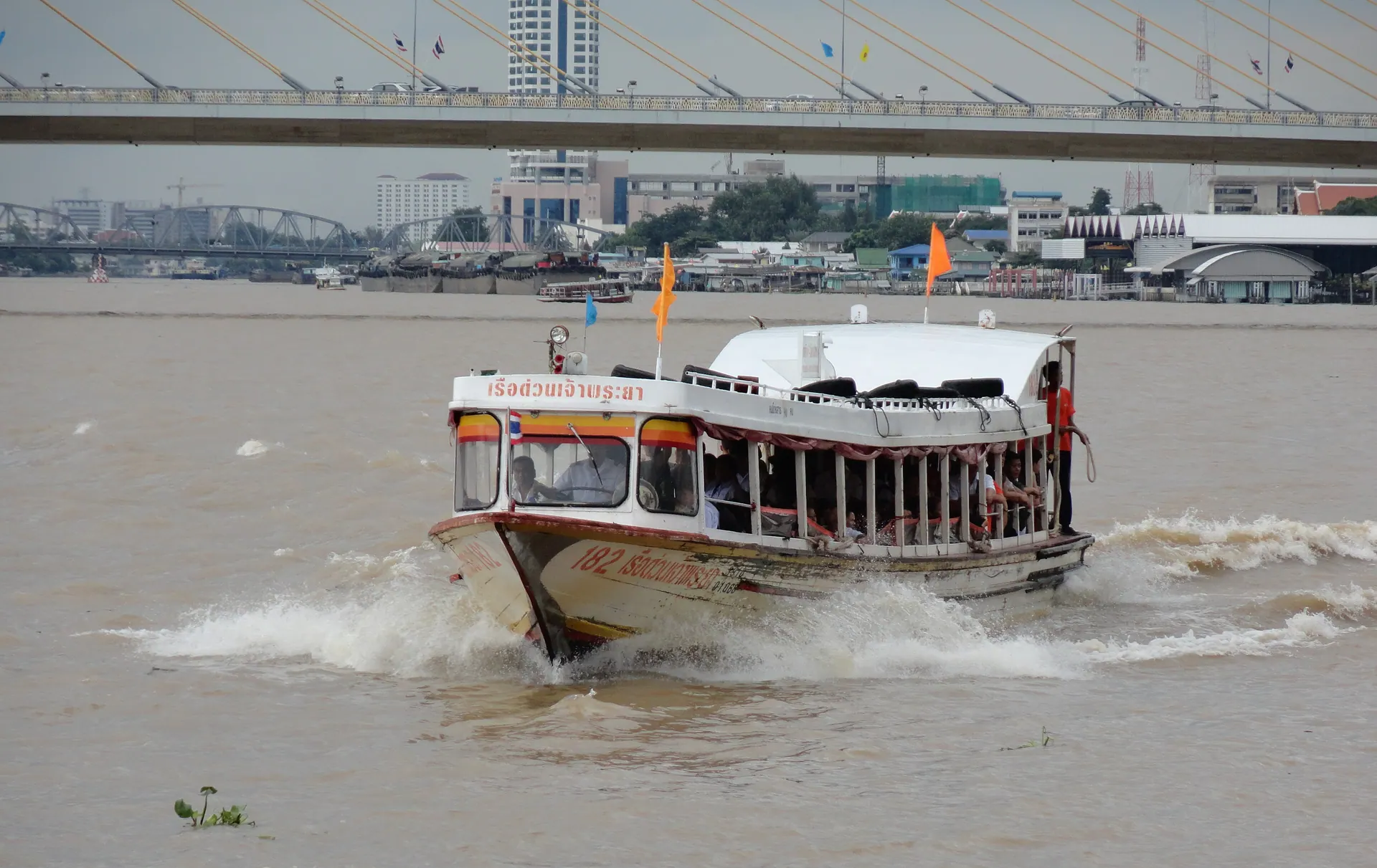 A Chao Phraya Express Boat crossing the river with a bridge behind