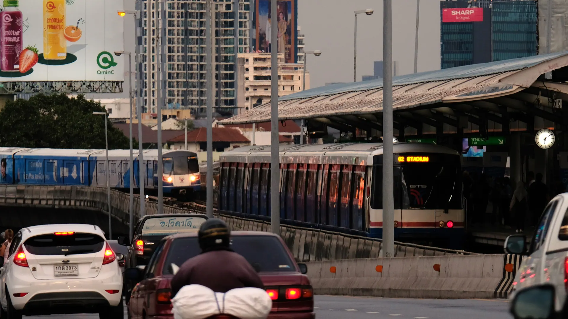 Two BTS trains at Saphan Taksin station, with road traffic below