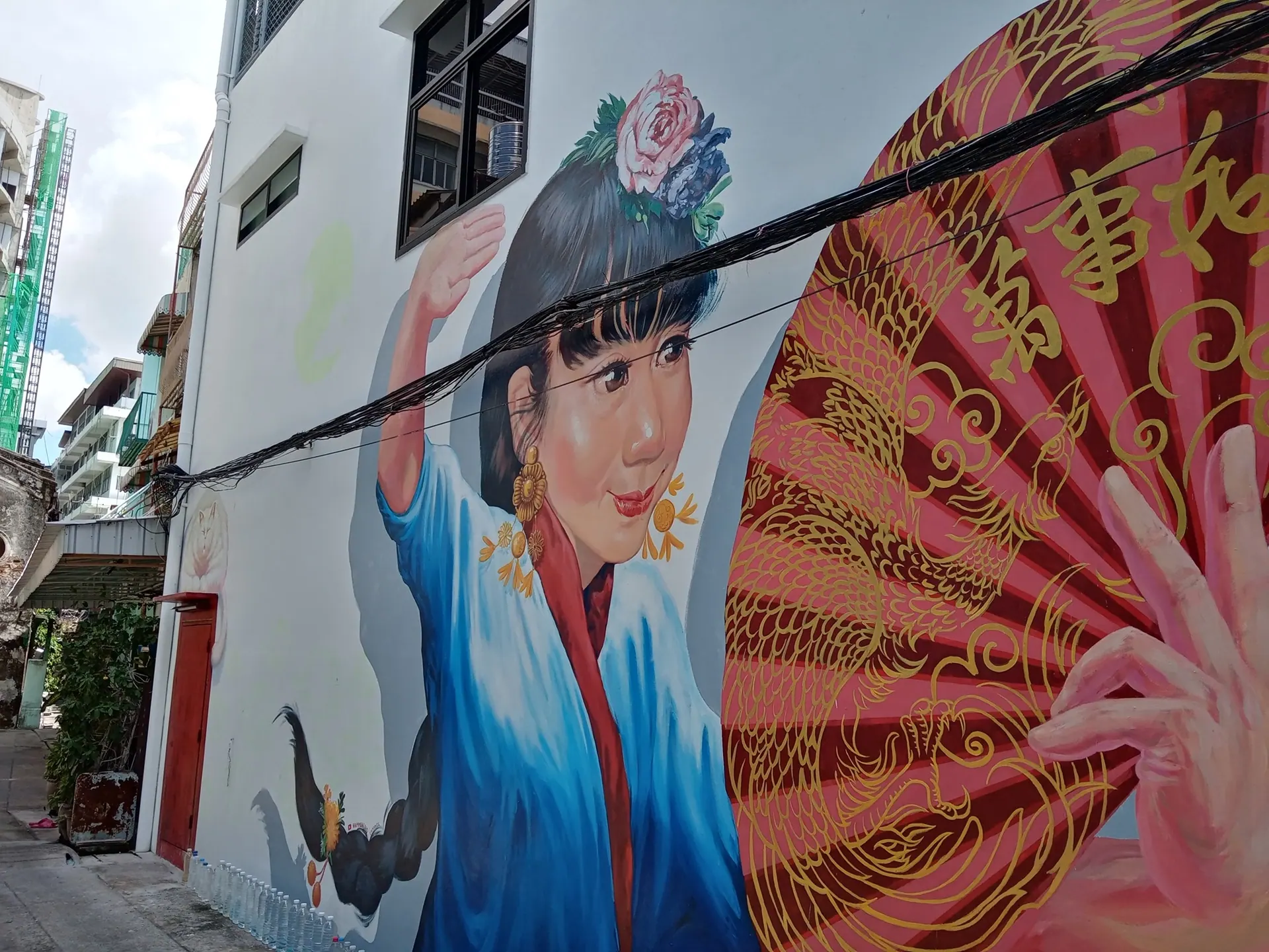 A painted mural of a woman with a red fan on a wall in Talat Noi