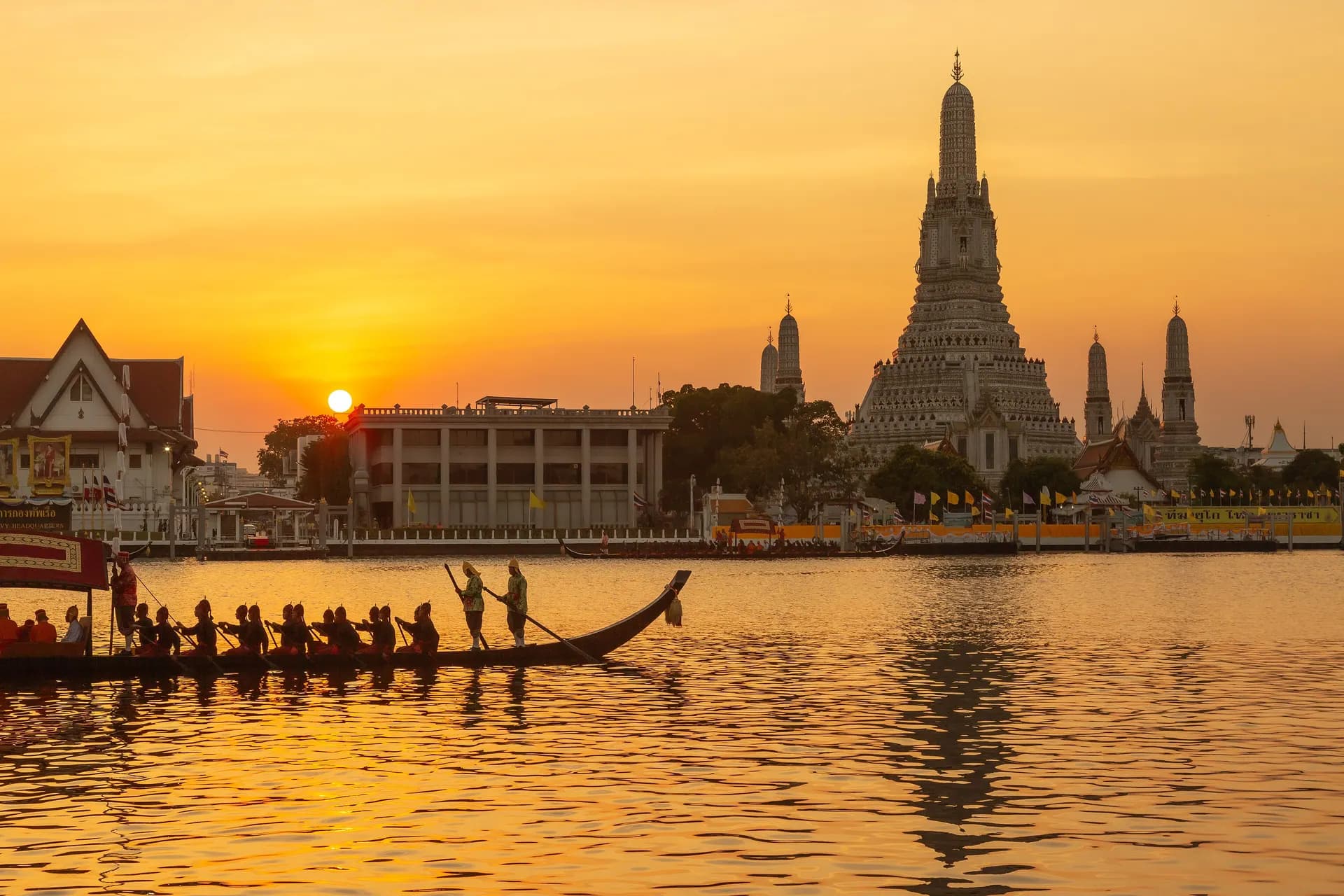 Wat Arun beside the Chao Phraya River at sunset with a long royal barge on the water