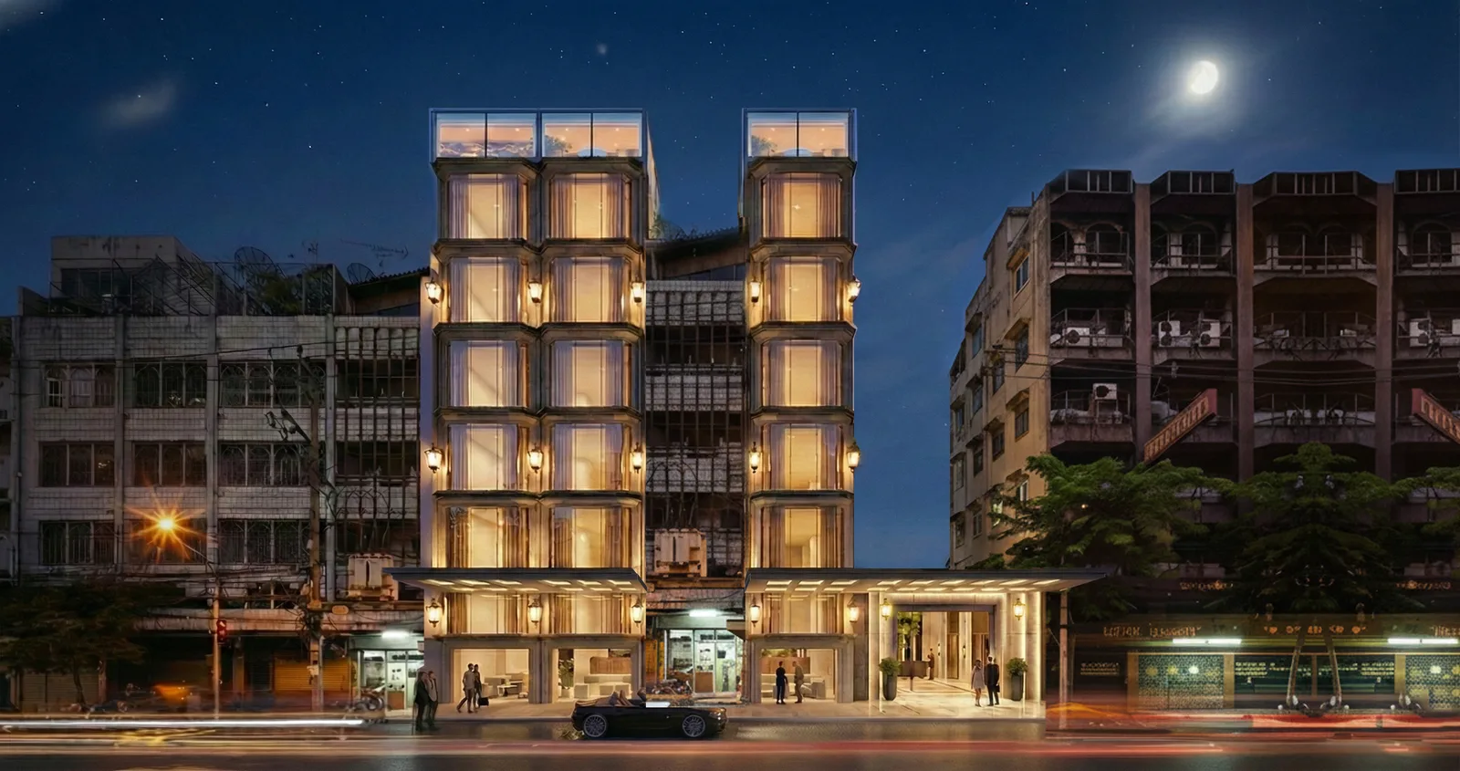 The hotel street elevation at dusk, its stacked bays lit from within above a covered ground-floor entrance